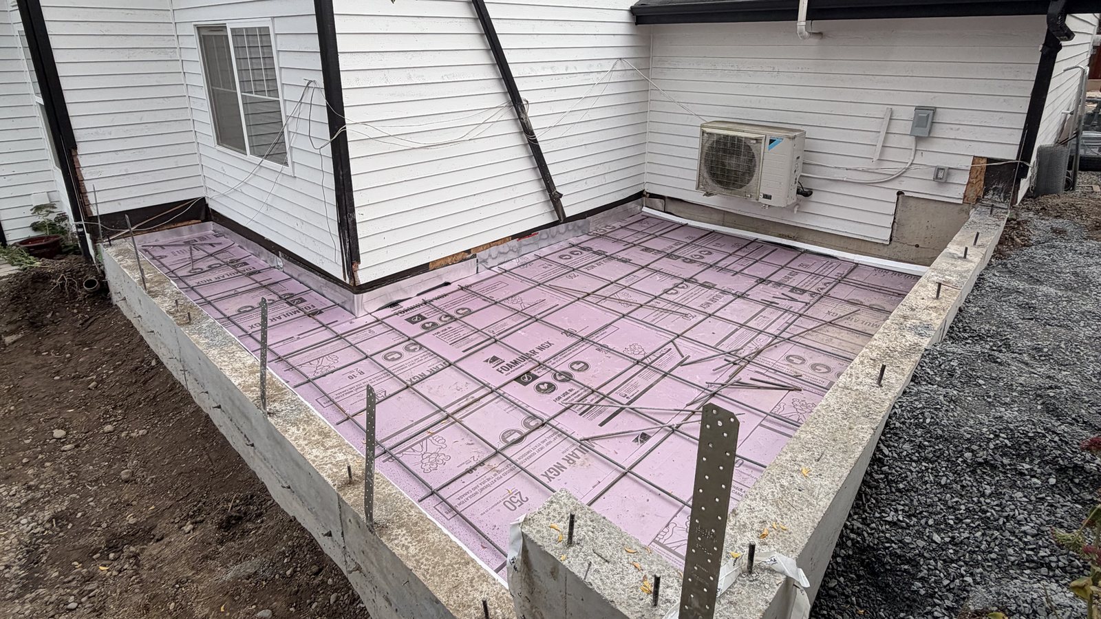 Stem walls, rigid insulation and slab rebar beside the existing house